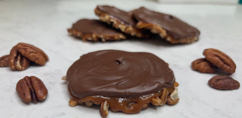 Chocolate-covered turtles with pecans on a white surface